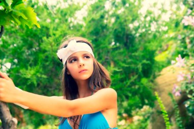 Yeşil çim ve ormanın arka planında mayo giymiş manken görünümlü bir kız. Seçici odaklanma. Beyaz saç bandı ve yay takan hoş bir bayan.