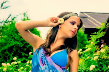 Yeşilliğe karşı poz veren güzel genç bir kadın ve mavi mendilli bir bungalov. Eşarplı ve bijouterie 'li zarif kız sahilde eğleniyor. Özgürlük ve tasasız kavram, Bali. bronzlaşma