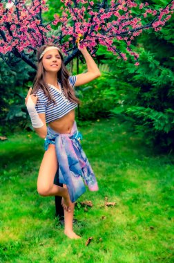 Kısa çizgili mavi beyaz gömlekli güzel esmer kız, parkta mayo ve gözenekli. Modaya uygun yaz cazibesi konsepti. Yaz yürüyüşü.