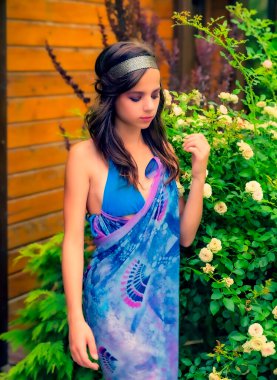 Yeşilliğe karşı poz veren güzel genç bir kadın ve mavi mendilli bir bungalov. Eşarplı ve bijouterie 'li zarif kız sahilde eğleniyor. Özgürlük ve tasasız kavram, Bali. bronzlaşma