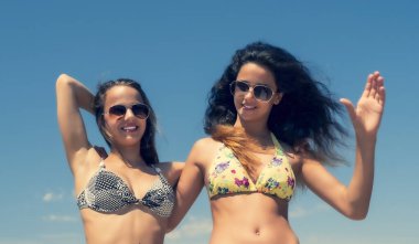 İki genç kadın sahilde dinleniyor. Gökyüzüne karşı parlak mayolu iki çekici genç arkadaş.