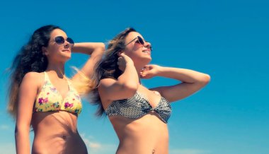 İki genç kadın sahilde dinleniyor. Gökyüzüne karşı parlak mayolu iki çekici genç arkadaş. Boşluğu kopyala