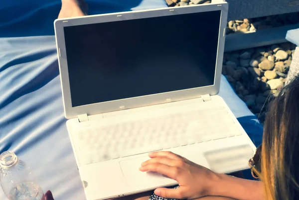 Young Woman Freelancer comfortable sitting at the chair on Ocean background, Using Laptop With Black Screen On The Beach. Girl Freelancer Working. Working outside office concept.