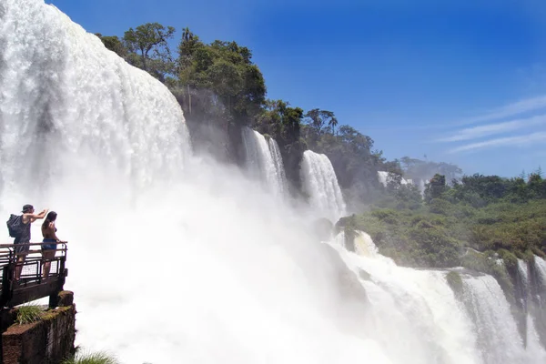 İnsanlar arka planda Iguazu Şelalesi 'ndeki San Martin düşüşünü görmek için podyumda yürüyorlar.