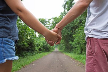 Arka planda doğa patikasıyla el ele tutuşurken yürüyen genç bir çift.