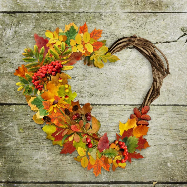 Uma grinalda de folhas de outono e bagas em forma de coração no fundo de madeira — Fotografia de Stock
