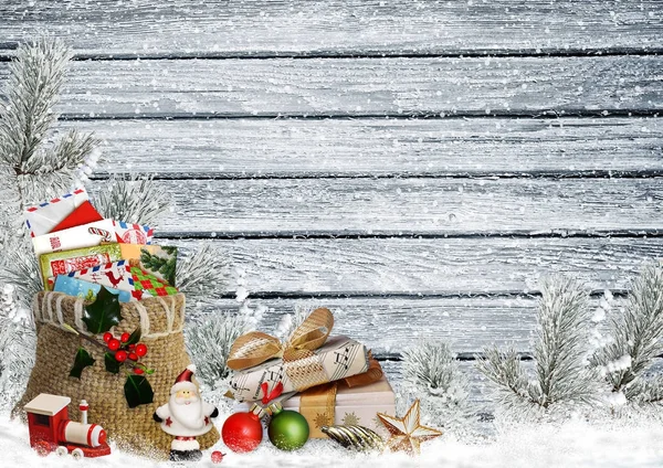 Biglietto di auguri natalizio con regali, una busta di lettere, Babbo Natale, giocattoli e rami di pino su una tavola di legno innevata — Foto Stock
