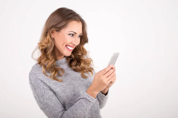 Mulher sorrindo e digitando no smartphone no estúdio lendo mídias
