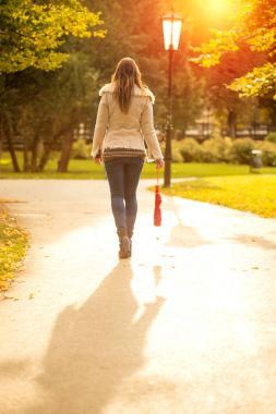 Kız gün batımında sonbaharda bir parkta yürüyüş