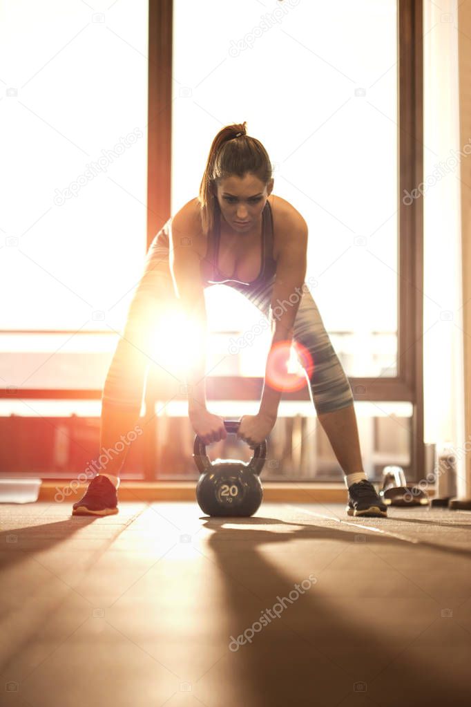Beautiful motivated woman working out with kettlebell at the gym