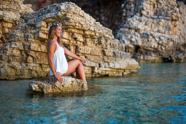 Mooie jonge vrouw zittend op een rots op het strand — Stockfoto