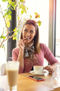 Güzel genç kadın gülümseyerek iken bir kafede bir çerez yemek