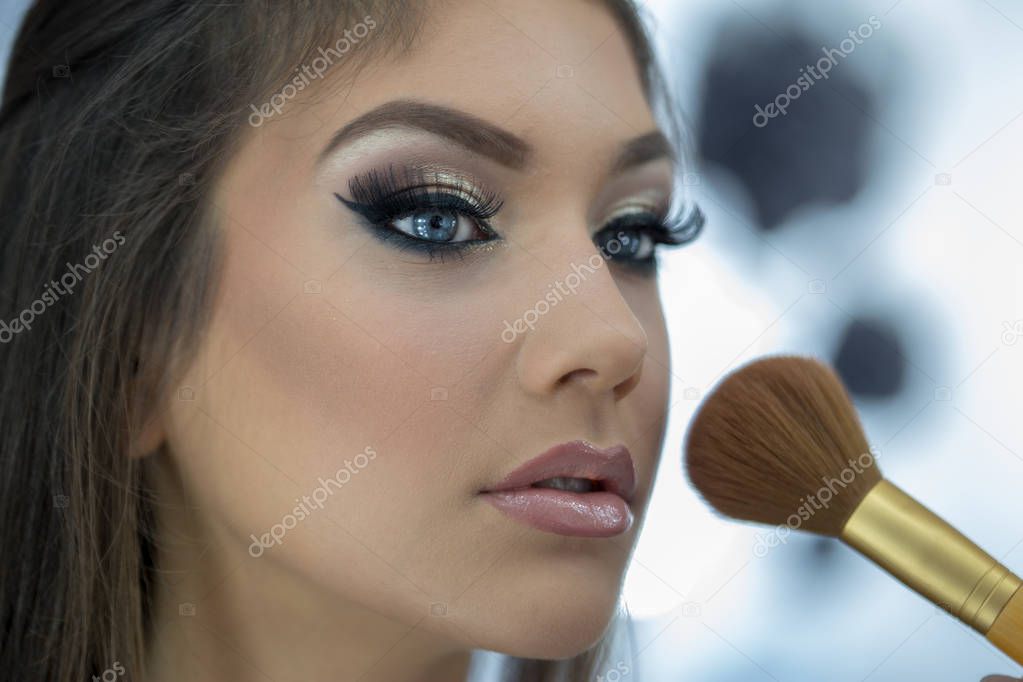 Beautiful young woman putting on make up in front of a mirror with a brush