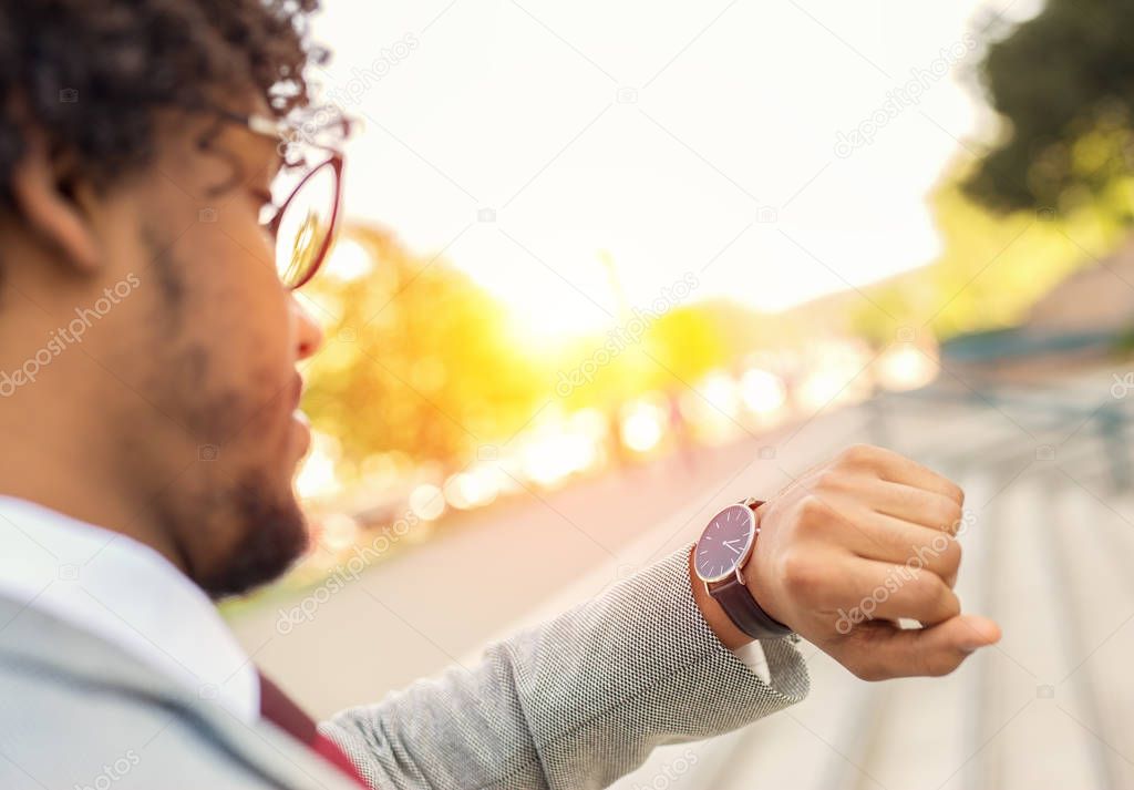 Handsome young business man talking on the phone while checking the time on his watch sunset