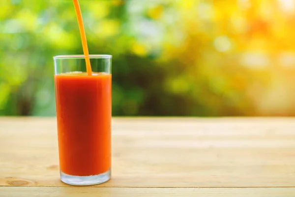 Pouring tomato juice into a glass on wooden table with blurred natural green background — Stock Photo, Image