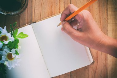 Kalem tutan ve çiçek ve kahve (renk süzgeç eklendi ve klasik sesi etkisi ile ahşap masa üzerinde bir günlük defterde yazılı el)