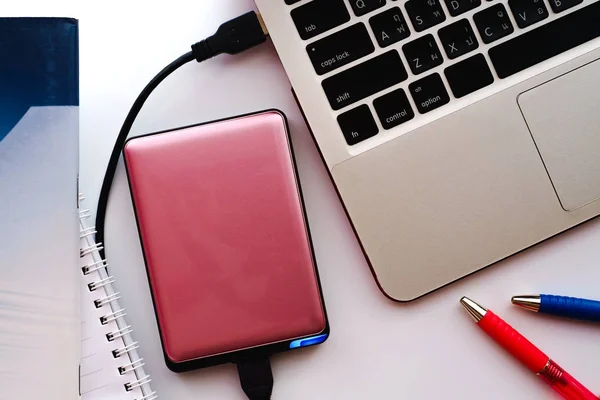 Spazio di lavoro con libri, penne e hard disk esterno rosa collegarsi al computer portatile — Foto Stock