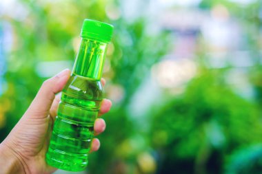 Yeşil şişe içme suyu karşı doğal arka plan bulanık tutan el