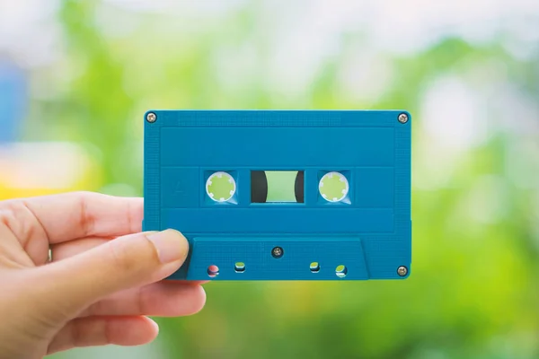 Hand holding a blue retro cassette tape against blurred background — Stock Photo, Image