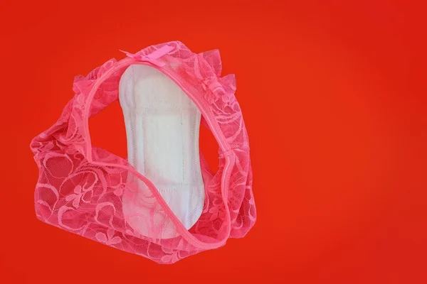 Calcinhas de renda feminina sexy rosa com guardanapo sanitário em backg vermelho — Fotografia de Stock