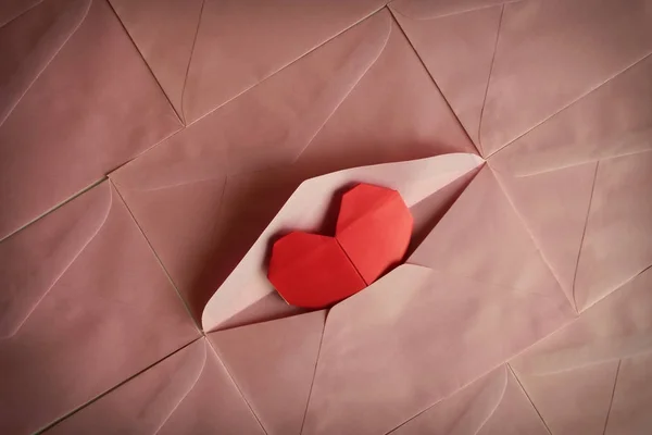 Червоний папір для серця орігамі на фоні рожевого конверта — стокове фото