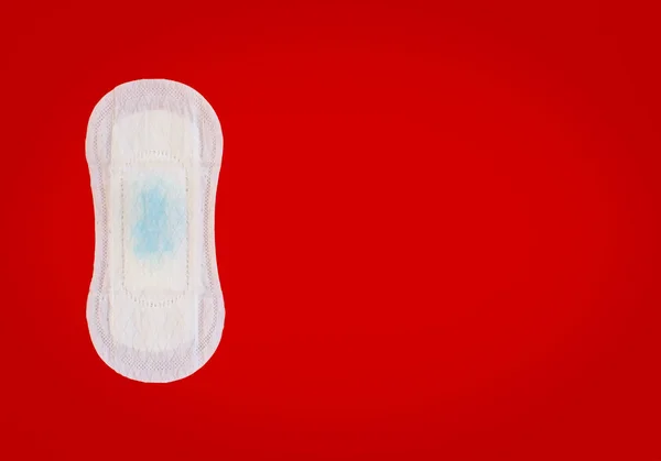 Guardanapo sanitário feminino com gotas líquidas azuis no fundo vermelho — Fotografia de Stock