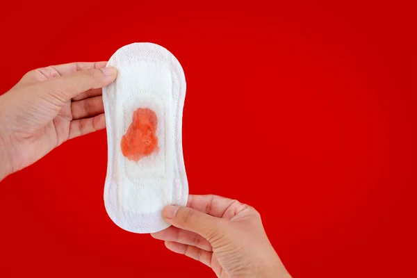 Mano que sostiene la servilleta sanitaria femenina con las gotas líquidas rojas en r — Foto de Stock