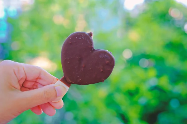 Handen håller hjärtat choklad glass på suddig naturlig grön — Stockfoto