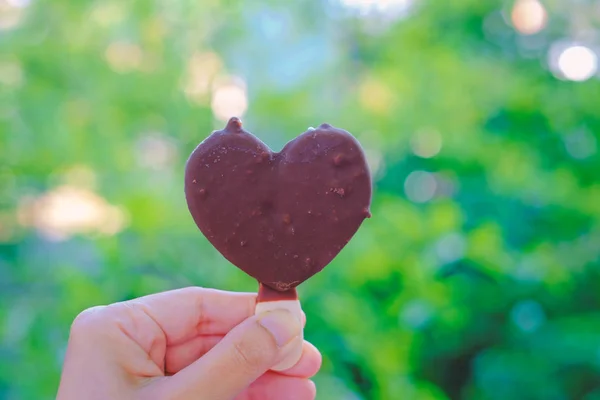 Handen håller hjärtat choklad glass på suddig naturlig grön — Stockfoto