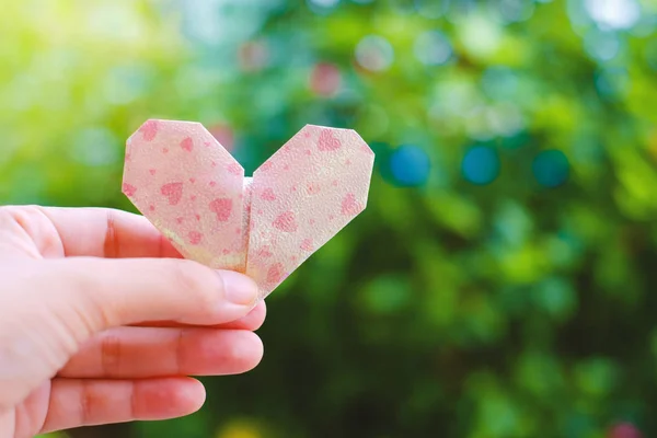 Mano sosteniendo papel corazón origami en borrosa verde natural backgr — Foto de Stock