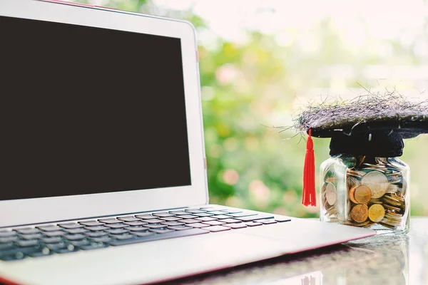 Computer laptop and square academic cap with the glass jar of co
