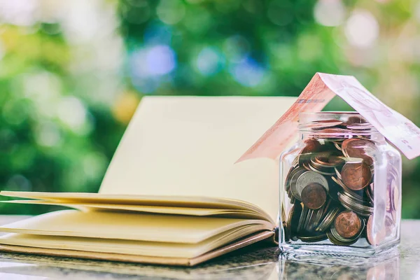 Techo de billetes cubrir el frasco de vidrio de dinero con cuaderno en blanco —  Fotos de Stock