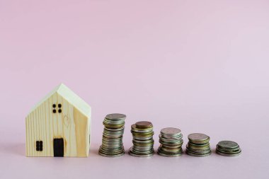 Ahşap ev modeli. Pembe arka planda madeni paralar. Fotokopi alanı da iş yeri ve emlak kavramı için finans alanı.