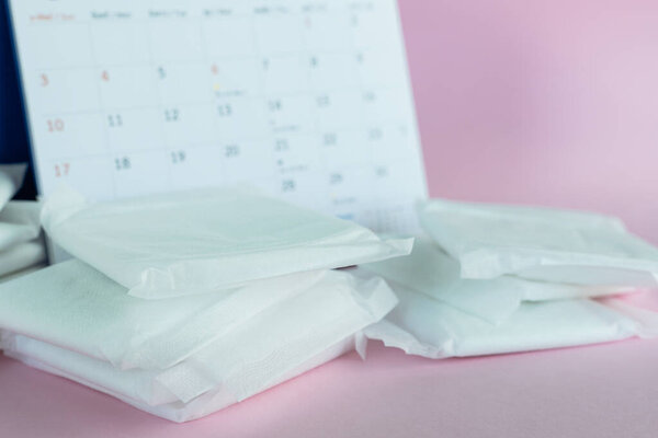 Feminine sanitary napkin, an absorbent item worn by a woman while menstruating, with blurred calendar on pink background for hygiene and health concept