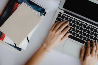 Üst görünüm, e-öğrenim, ev ve çalışma alanı konsepti için beyaz ofis masasında bir yığın kitapla bilgisayar dizüstü bilgisayar kullanıyor.