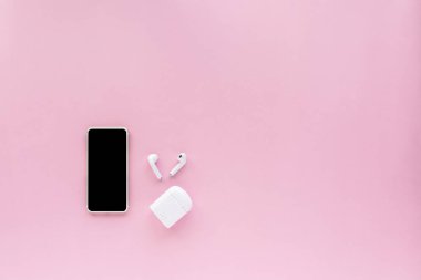 Pembe arka planda kablosuz kulaklıklı akıllı telefon. Medya teknolojisi ve modern yaşam tarzı konsepti için kopyalama alanı var.