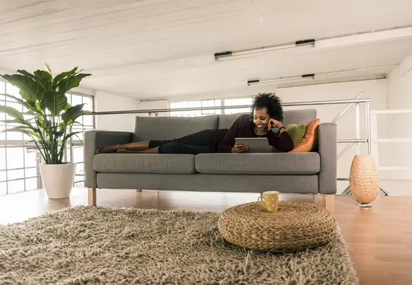 Frau liegt mit Tablet auf Couch — Stockfoto