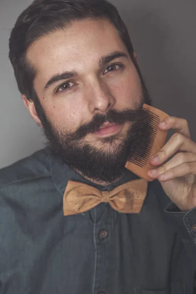 Мужчина расчесывает бороду деревянной расчёской — стоковое фото