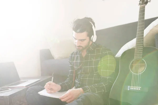 Homem em fones de ouvido escrevendo notas — Fotografia de Stock