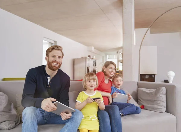 Família Segurando Dispositivos Móveis Sofá Casa — Fotografia de Stock