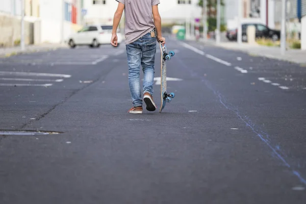 男孩背着滑板在街上的背观 — 图库照片