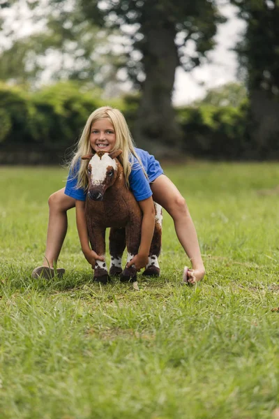 Sonriente Chica Edad Elemental Sentado Caballo Juguete Prado Verde —  Fotos de Stock