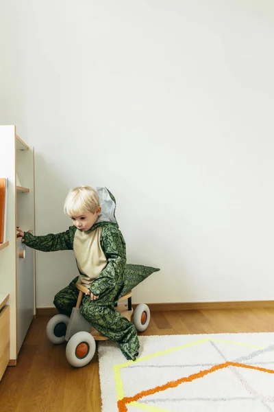 小男孩穿着恐龙服装坐在家里的玩具车上 — 图库照片