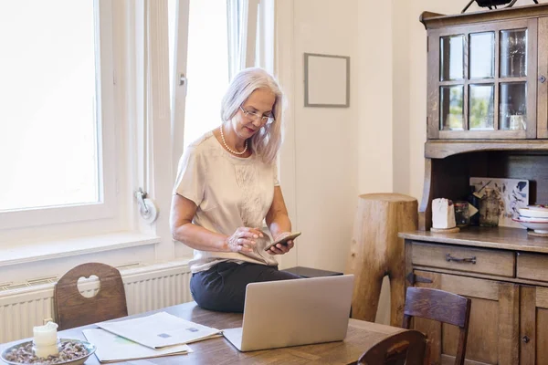 Businesswoman working at home office with smartphone and laptop — Stock Photo