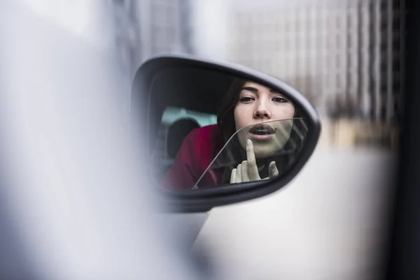 Jolie femme assise en voiture appliquant le maquillage dans le miroir d'aile — Photo de stock