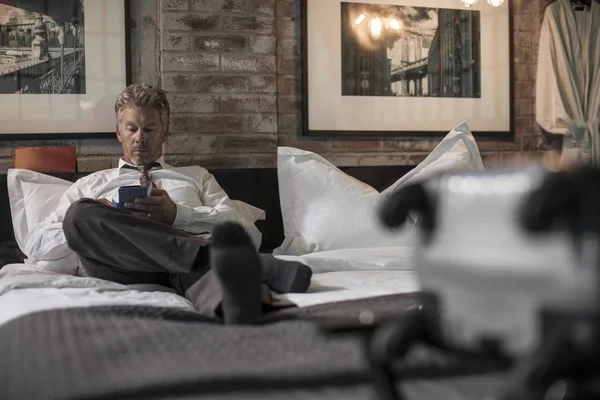 Businessman using smartphone on bed in hotel room — Stock Photo