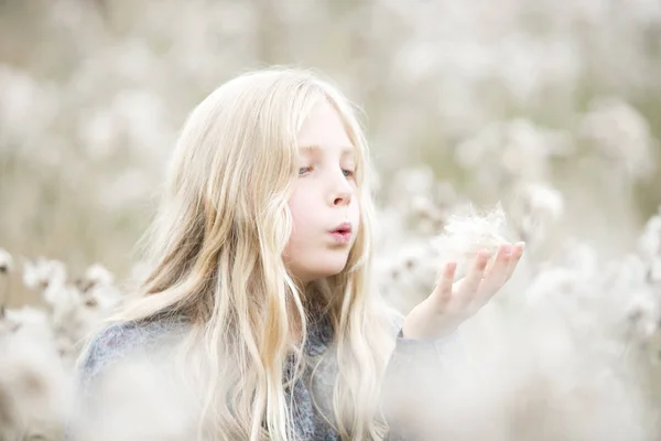 Retrato de menina de pé em um campo soprando sementes para fora de sua mão — Fotografia de Stock