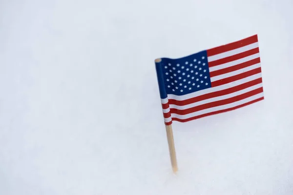 Small United State of America flag made from paper with brown toothpick on white snow background.