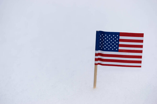 Small United State of America flag made from paper with brown toothpick on white snow background.