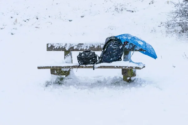 stock image wooden bench chair in a park completely cover with snow after a blizzard during the winter christmas holidays, a backpack bag, umbrella, camera tripod and a small bag on the chair.